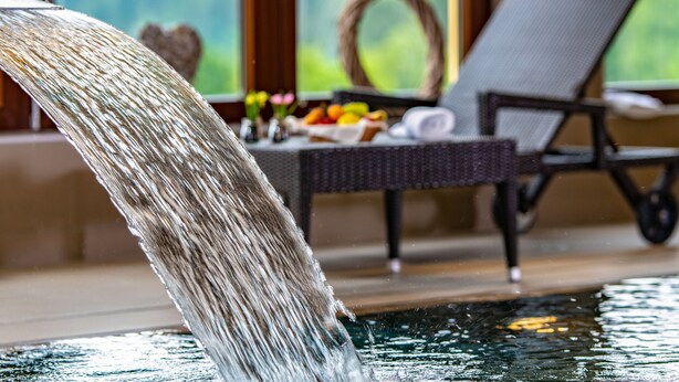 Una fuente con una cascada, una silla de mimbre para relajarse y una mesa con frutas y flores.