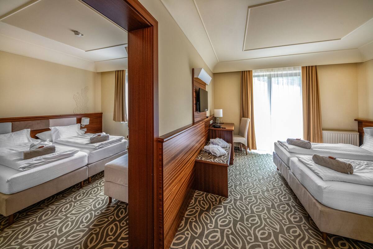 A hotel room with two beds, a desk, a chair, and a television.