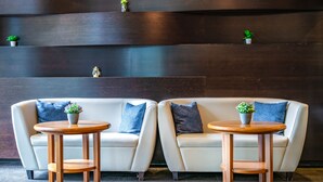 Un área de estar moderna con dos sofás y dos mesas redondas de madera, cada una con una pequeña planta en maceta.