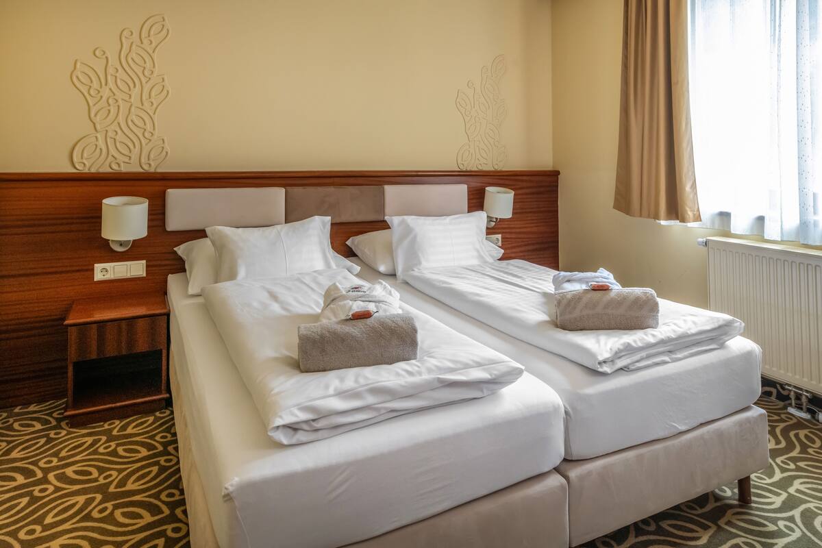 A hotel room with two beds, wooden headboards, white linens, and decorative wall art.