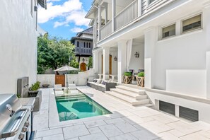 Un espace piscine extérieur moderne, doté d’un barbecue, de sièges et d’un escalier menant à un patio couvert.