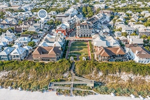 Vue aérienne d’un quartier résidentiel, avec un bâtiment rouge imposant, une pelouse bien entretenue et un accès à la plage agrémenté d’une promenade en bois.