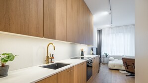 A modern kitchen with wooden cabinets, a white countertop, and a sink. There is a dining area with a sofa and a chair. - Nordic townhouse with own sauna at the city center of Helsinki (Helsinki)