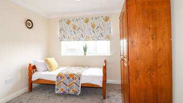 A room with a bed, a wooden wardrobe, a window with a plant, and a ceiling light.