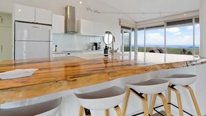 A modern kitchen with a wooden countertop, white bar stools, and a view of the landscape through large windows.