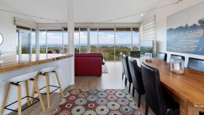 A modern kitchen with a bar area, a dining table with chairs, a red sofa, and a large window offering a scenic view.