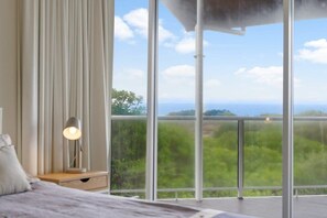 Enjoy a panoramic view of the lush landscape and sea from the comfort of this serene bedroom.
