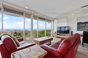 Un soggiorno moderno con una grande TV, divani in pelle, un tavolino in legno e ampie finestre che offrono vista sul paesaggio.