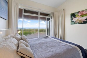A bedroom with a large bed, a view through a sliding glass door, and a painting of flowers on the wall.