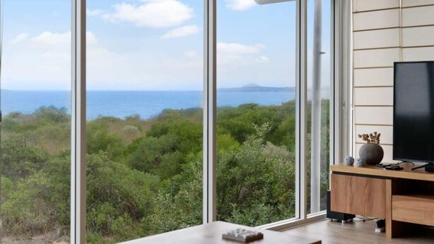 A room with large windows offering a view of the sea and greenery.