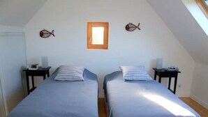 Ein Zimmer mit zwei Einzelbetten, einem kleinen Fenster und Wandbildern mit Fischmotiven.