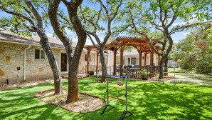 A stone building with a covered patio area, a swing set, and a well-maintained lawn. - Peaceful Retreat near Lake Travis & Volente (Volente)