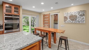 A kitchen with granite countertops, stainless steel appliances, wooden cabinets, and a large island with stools. - Peaceful Retreat near Lake Travis & Volente (Volente)