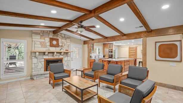 A spacious living area with a stone fireplace, wooden ceiling beams, and a kitchen in the background. - Peaceful Retreat near Lake Travis & Volente (Volente)