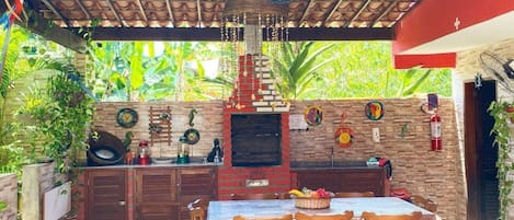 Un área de cocina al aire libre con horno de ladrillo, sillas de madera y una mesa.