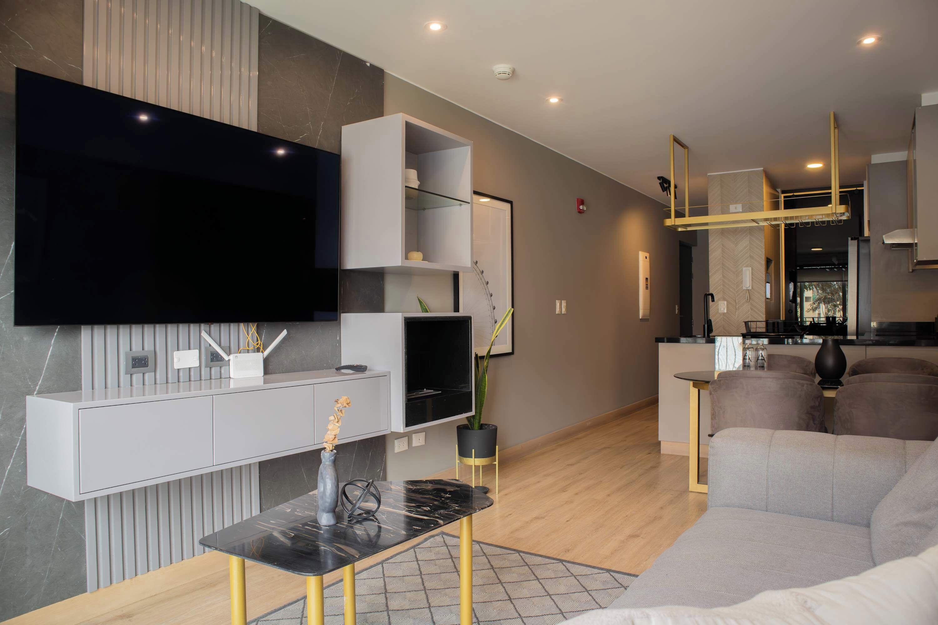 Un salon moderne doté d’un téléviseur à écran plat, d’un canapé gris et d’un coin repas avec une table et des chaises noires.