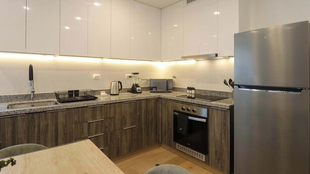 Una cocina moderna con armarios blancos, un refrigerador de acero inoxidable, horno empotrado y microondas.