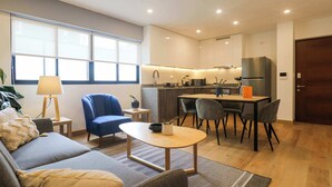 Una sala de estar moderna con un sofá, una mesa de centro y un comedor con sillas, y una cocina al fondo.