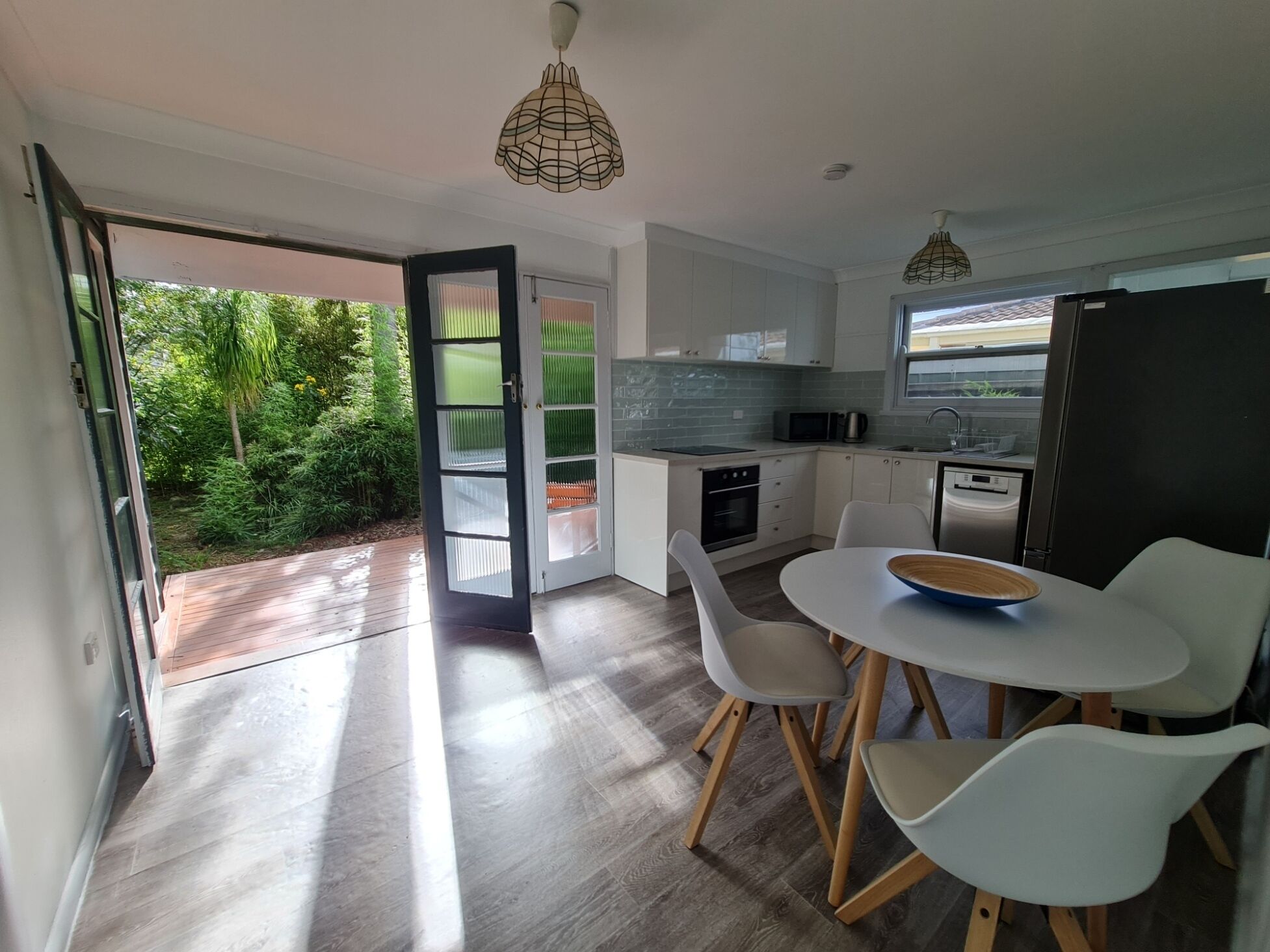 A modern kitchen with white cabinets, a black refrigerator, and a dining area with white chairs.
