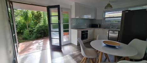 Uma cozinha moderna com armários brancos, uma geladeira preta e um espaço de refeições com cadeiras brancas.