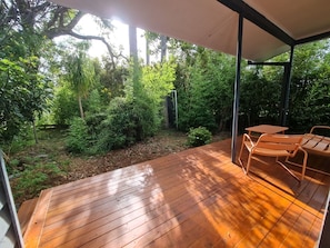 Une terrasse en bois dotée d’un espace salon abrité, entourée d’une végétation luxuriante et d’arbres.