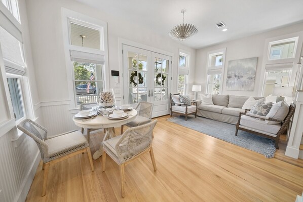 A spacious living area with a wooden floor, a round dining table with chairs, a sofa, and a chandelier.