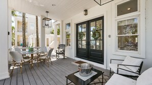 A covered patio with a dining table and chairs, a black door with glass panels, and a white wall with a window. - Stella By The Sea 3 Bedroom Home by RedAwning (Panama City Beach)