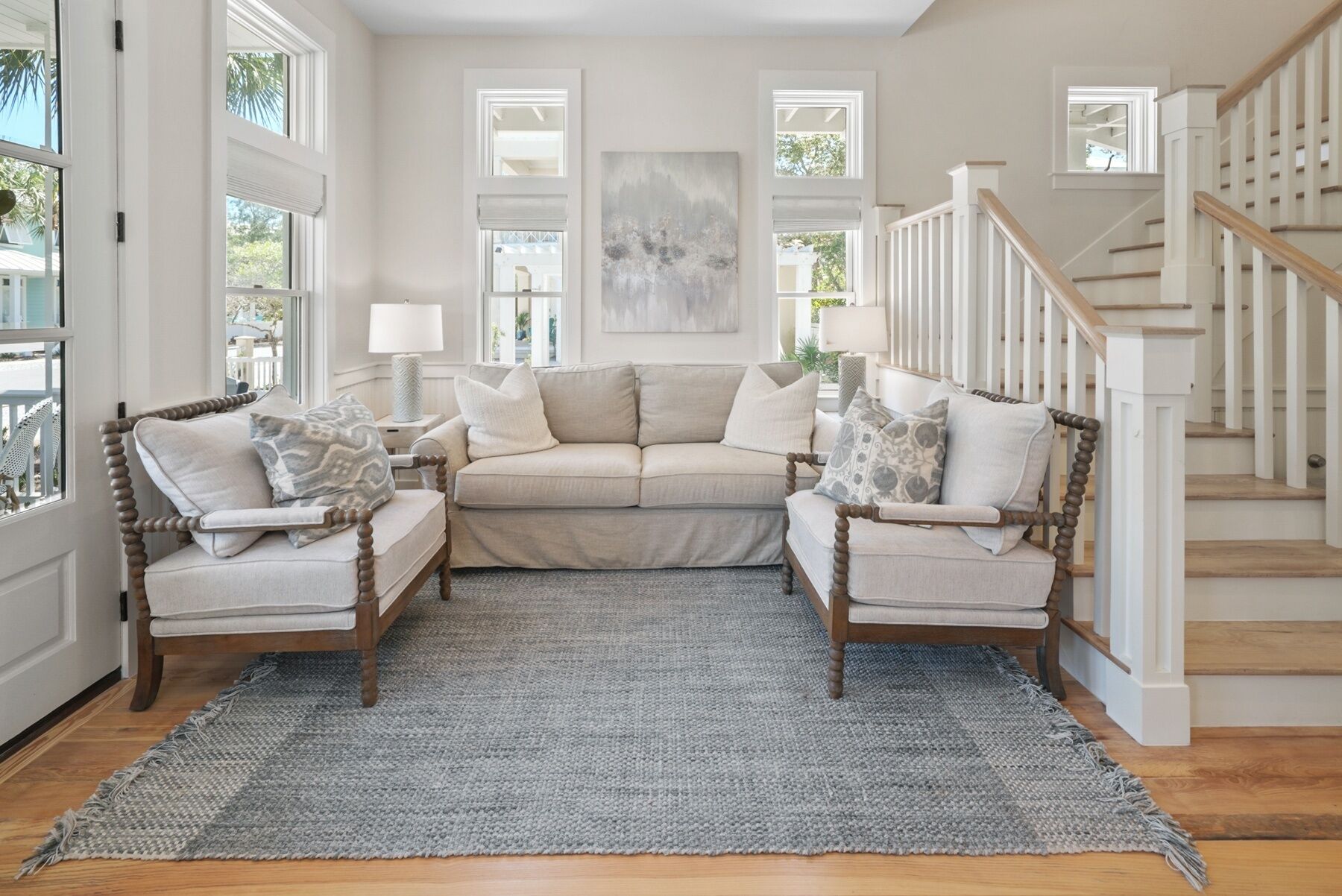 A living room with a beige sofa, two armchairs, a grey rug, and a staircase.