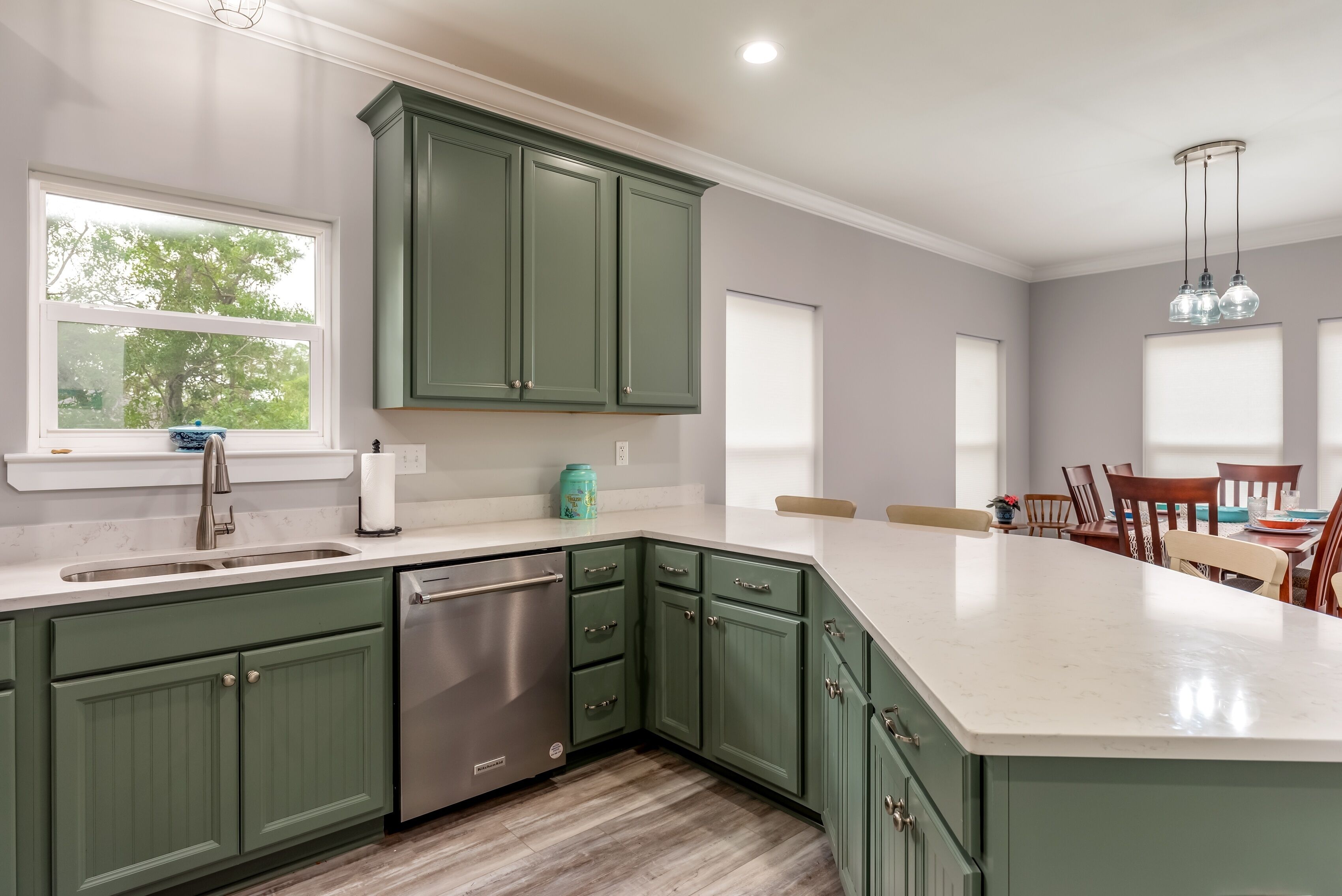 A kitchen with green cabinets, a stainless steel dishwasher, and a large island.
