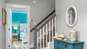 A staircase with a wooden handrail and white balusters, leading to a bedroom with a bed and a nightstand. - Blue Haven - 1414 Oleander 4 Bedroom Home by RedAwning (Dauphin Island)