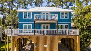 A two-story blue house with a wooden deck and a balcony. - Blue Haven - 1414 Oleander 4 Bedroom Home by RedAwning (Dauphin Island)