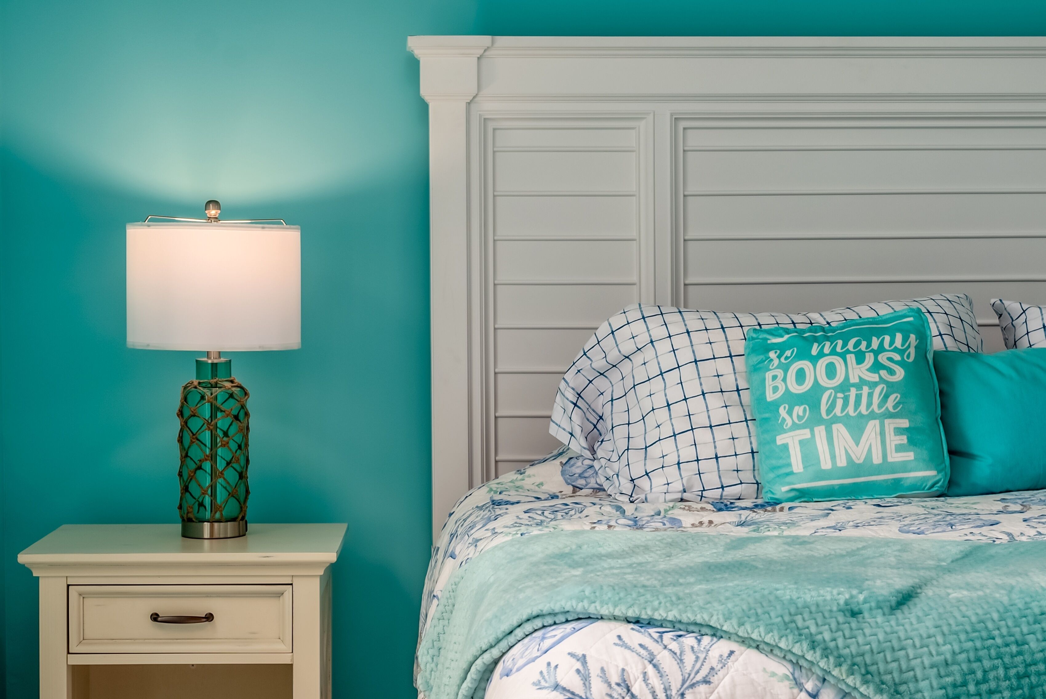 Une chambre avec des murs de couleur turquoise, une table de chevet blanche avec une lampe, un lit avec un oreiller turquoise et une couverture turquoise.