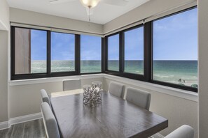 Uma sala de jantar com uma mesa grande e cadeiras, grandes janelas com vista para o oceano e um ventilador de teto.