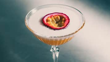 A martini glass with a rim of crushed ice and a passion fruit garnish on a reflective surface.