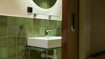 Un baño con azulejos verdes, un lavamanos blanco, una repisa de vidrio y un espejo sobre el lavamanos.