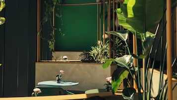 Una habitación con una pared verde, un espejo redondo y un estante de madera con plantas.
