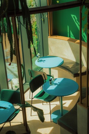 A modern interior with round tables and chairs, a bench, and a view through a window with greenery outside. - Poppies (Amsterdam)
