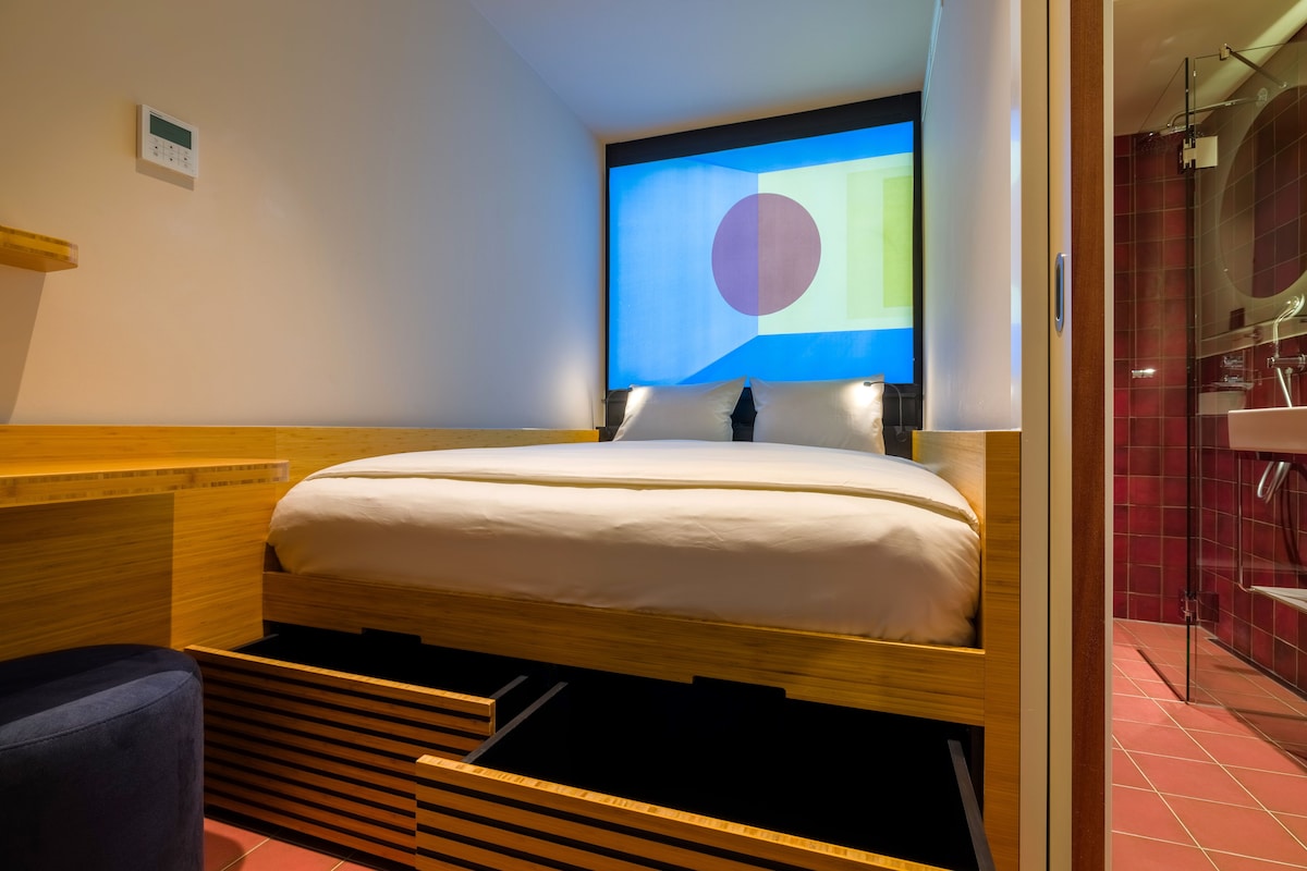 A hotel room with a bed, a wooden headboard, a wall-mounted TV, and a bathroom visible through an open door.