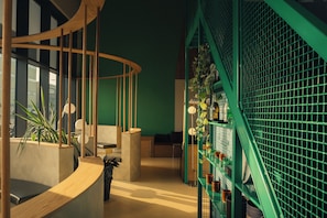 Un intérieur moderne avec un escalier en colimaçon, des coins salon et un mur végétal orné d’un motif en réseau.