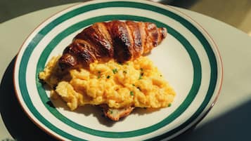 Une assiette contenant des œufs brouillés et un croissant, posée sur une table dont le bord est orné de rayures.