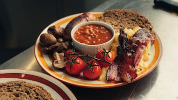 Un plato de comida para el desayuno con huevos, tocino, champiñones, tomates y tostadas.