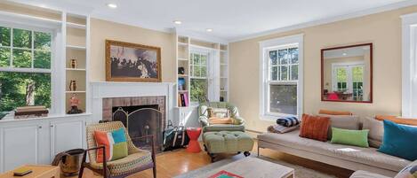 A well-lit living room with a fireplace, seating area, and bookshelves.