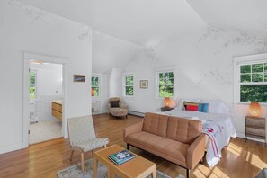 A spacious room with a bed, a sofa, a chair, and a small table. There are windows allowing natural light and a view of greenery outside. - Classic Stockbridge Cottage (Stockbridge)