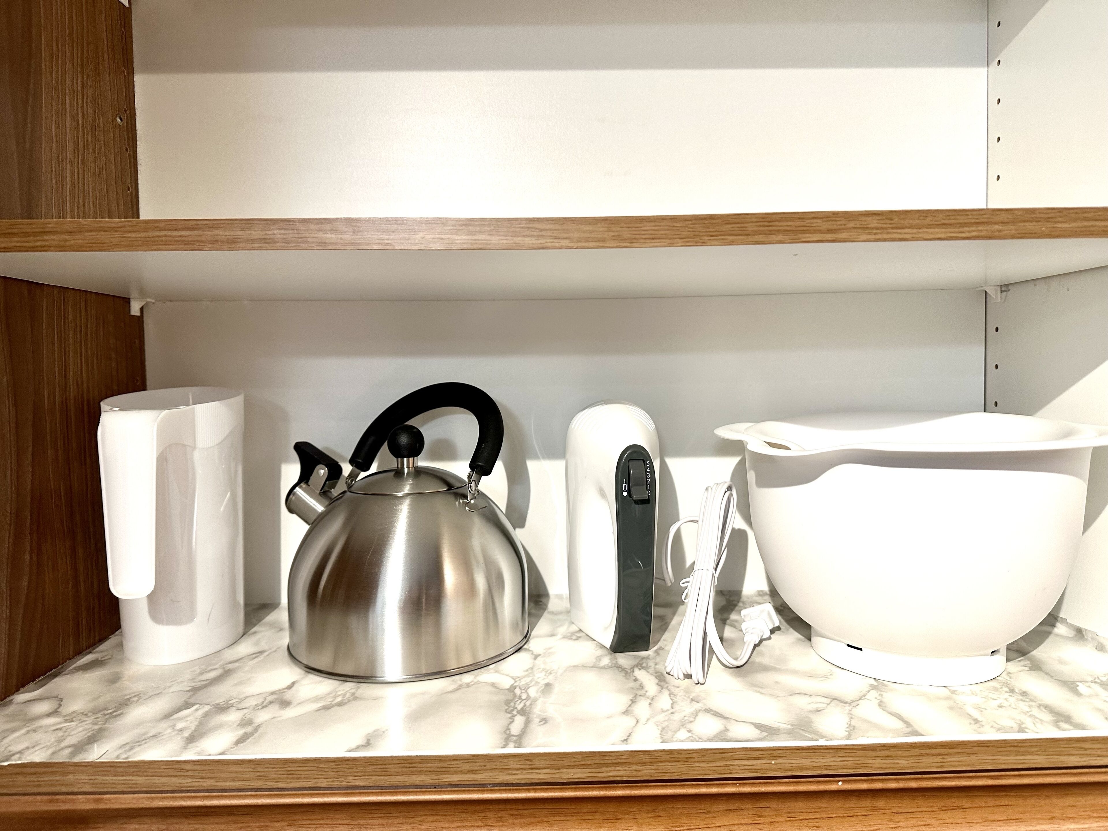 Uma prateleira na cozinha com uma chaleira de aço inoxidável, uma caneca branca, uma chaleira elétrica branca e uma tigela branca.