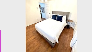 A bedroom with a bed, a ceiling fan, a nightstand, and a door leading to another room. - The Extravagant Minimalist (Gatineau)