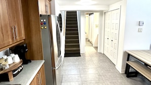 A modern kitchen with wooden cabinets, a stainless steel refrigerator, and a built-in oven. A staircase leads to another level. - The Extravagant Minimalist (Gatineau)
