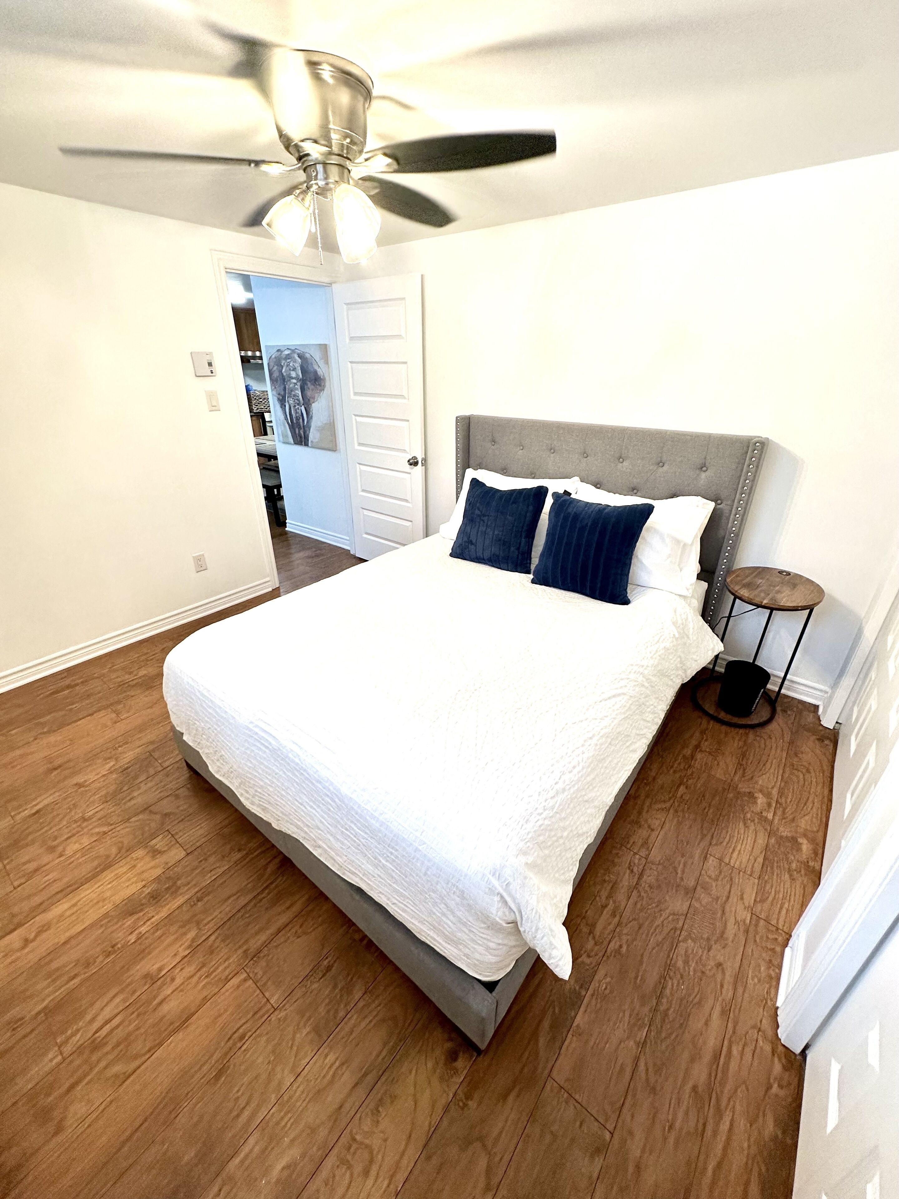 A bedroom with a bed, a ceiling fan, and a door leading to another room.