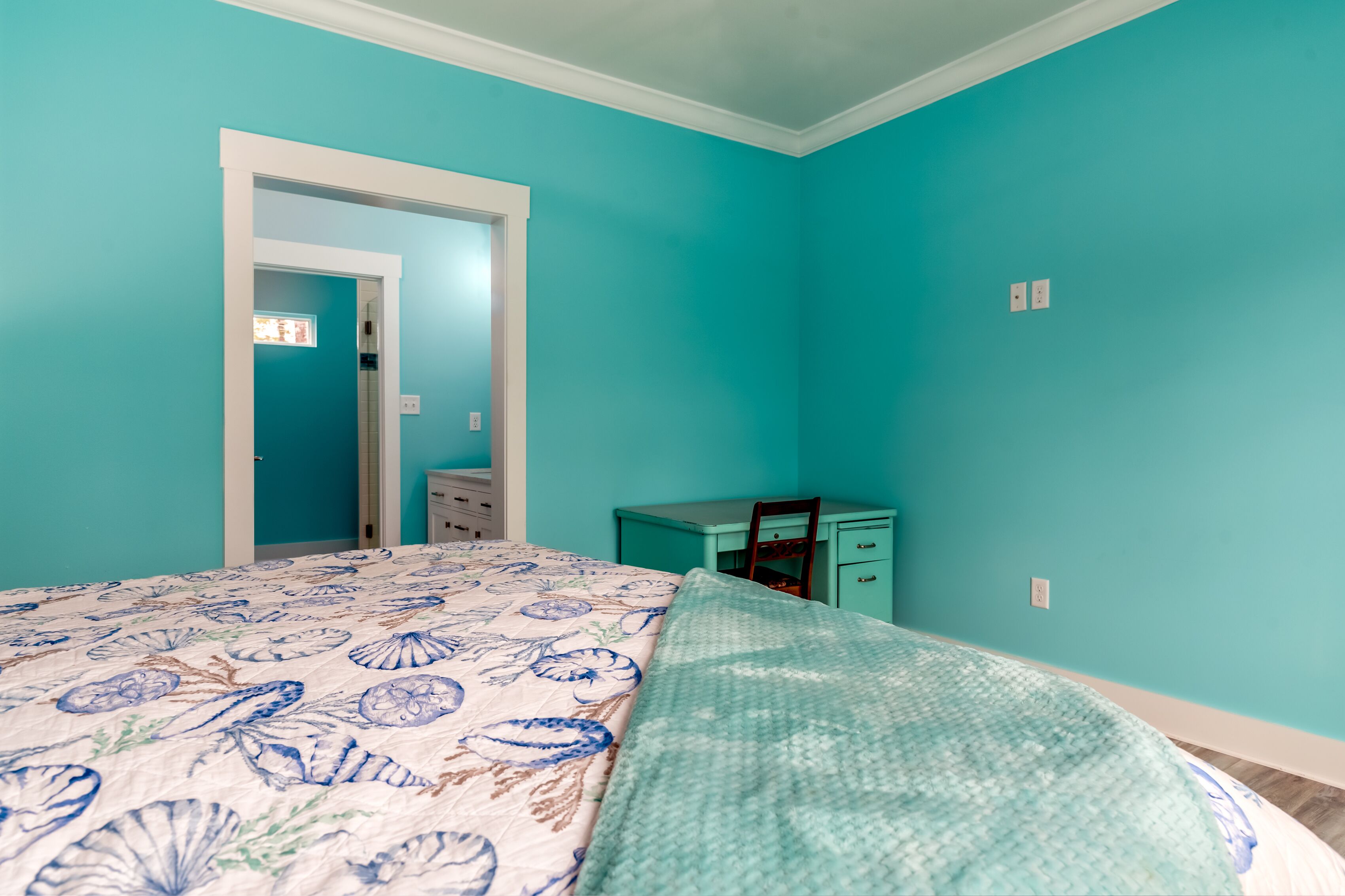 Un dormitorio con paredes color turquesa, una cama con colcha estampada, un escritorio y una silla.