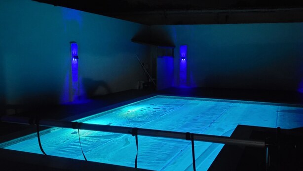 Une grande piscine rectangulaire dotée d’un fond en verre, entourée de murs sur lesquels sont fixés des luminaires verticaux.