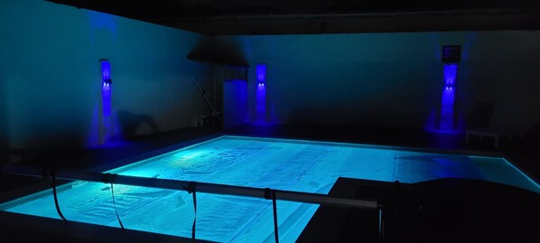 Une grande piscine rectangulaire dotée d’un fond en verre, entourée de murs sur lesquels sont fixés des luminaires verticaux.